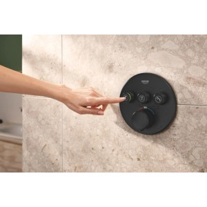 Runder, schwarzer Grohe SmartControl Thermostat an gefliester Wand. Hand drückt Taste für Duschfunktion. Modernes Badezimmer.