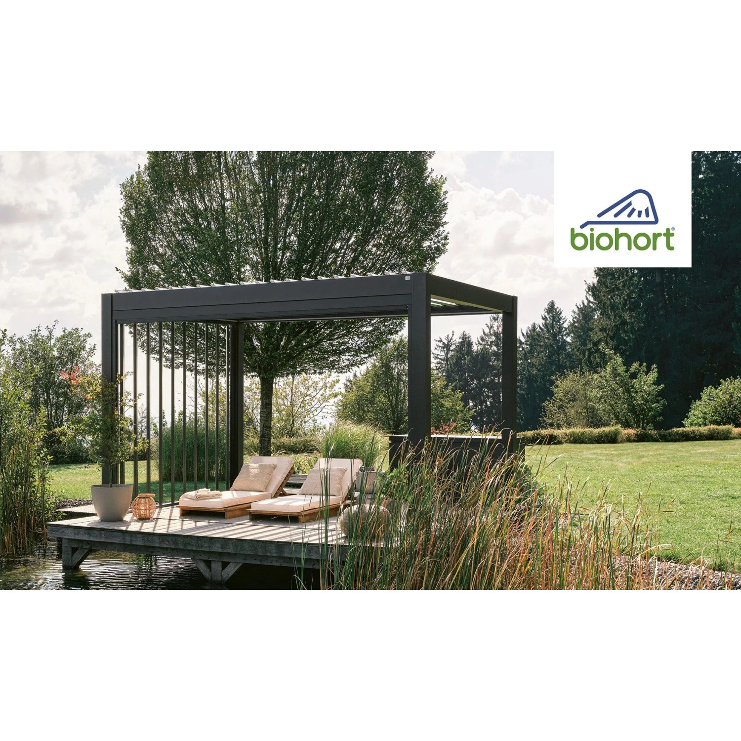 Biohort Pergola 4,5x3,5m in Quarzweiß auf Holzdeck mit zwei Liegen im Garten.
