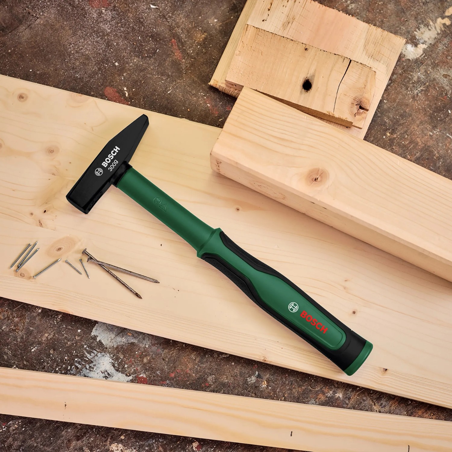 Bosch Schlosserhammer (300g) auf Holz mit Nägeln. Hammer mit grünem Griff.