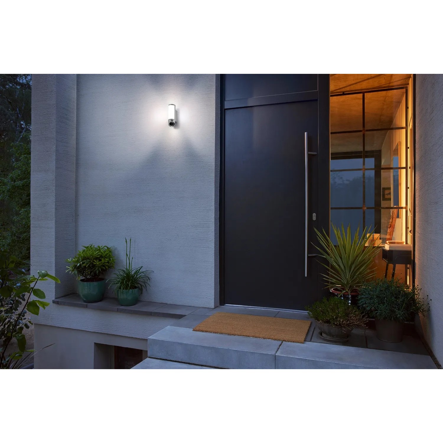 Bosch Smart Home Eyes II Außenkamera in Silber an Hauswand mit Tür und Pflanzen.