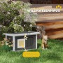 Graues Outdoor-Katzenhaus aus Tannenholz mit weißem Rand und gelber Kratzmatte auf grünem Rasen. Eine Katze sitzt daneben.