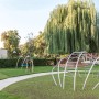 Rote Rasengitter Fallschutzplatte 100x100x4,5 cm auf Spielplatz mit Geräten und Baum.