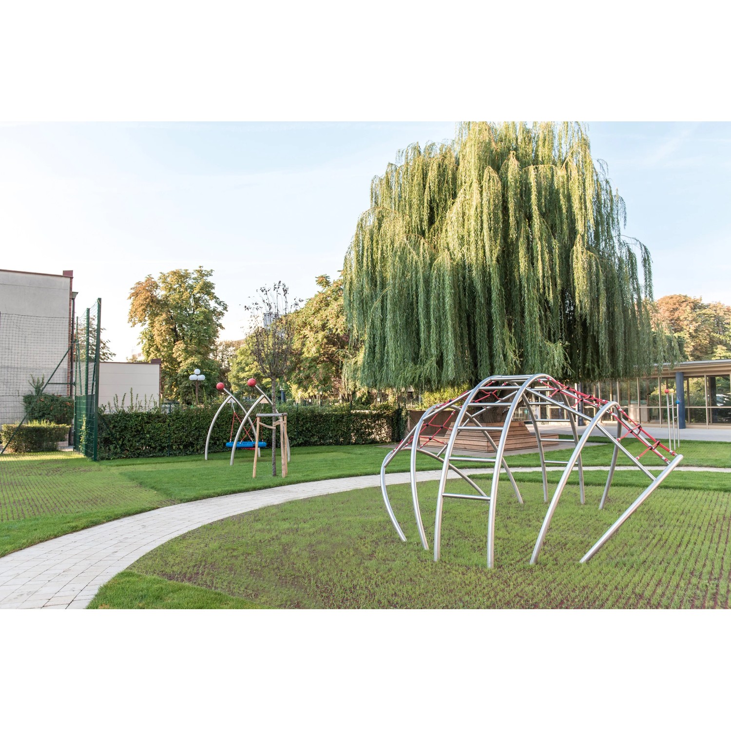 Rote Rasengitter Fallschutzplatte 100x100x4,5 cm auf Spielplatz mit Geräten und Baum.