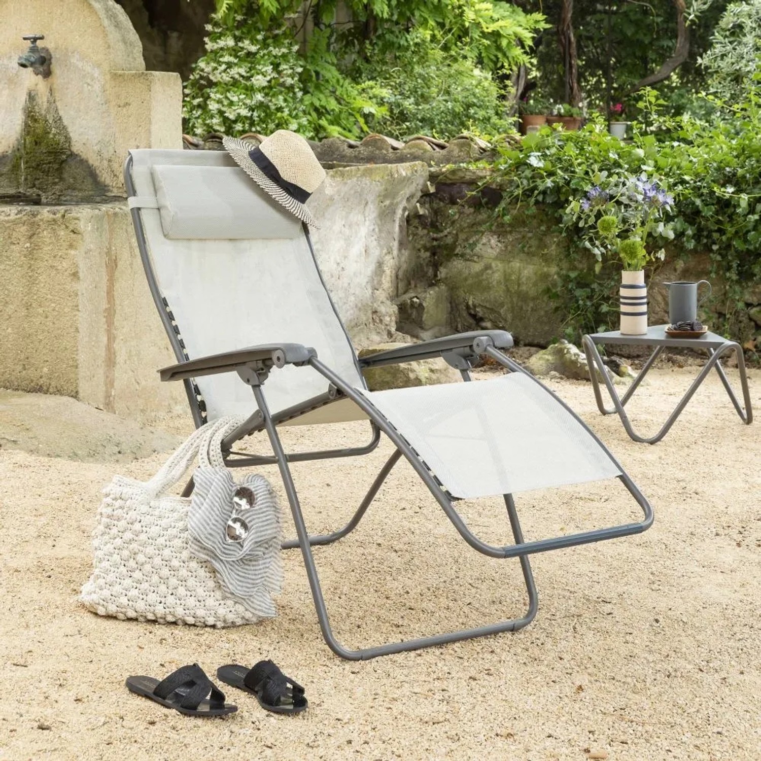 Lafuma Relaxsessel RSXA CLIP Batyline® Seigle II im Garten mit Tasche und Hut.