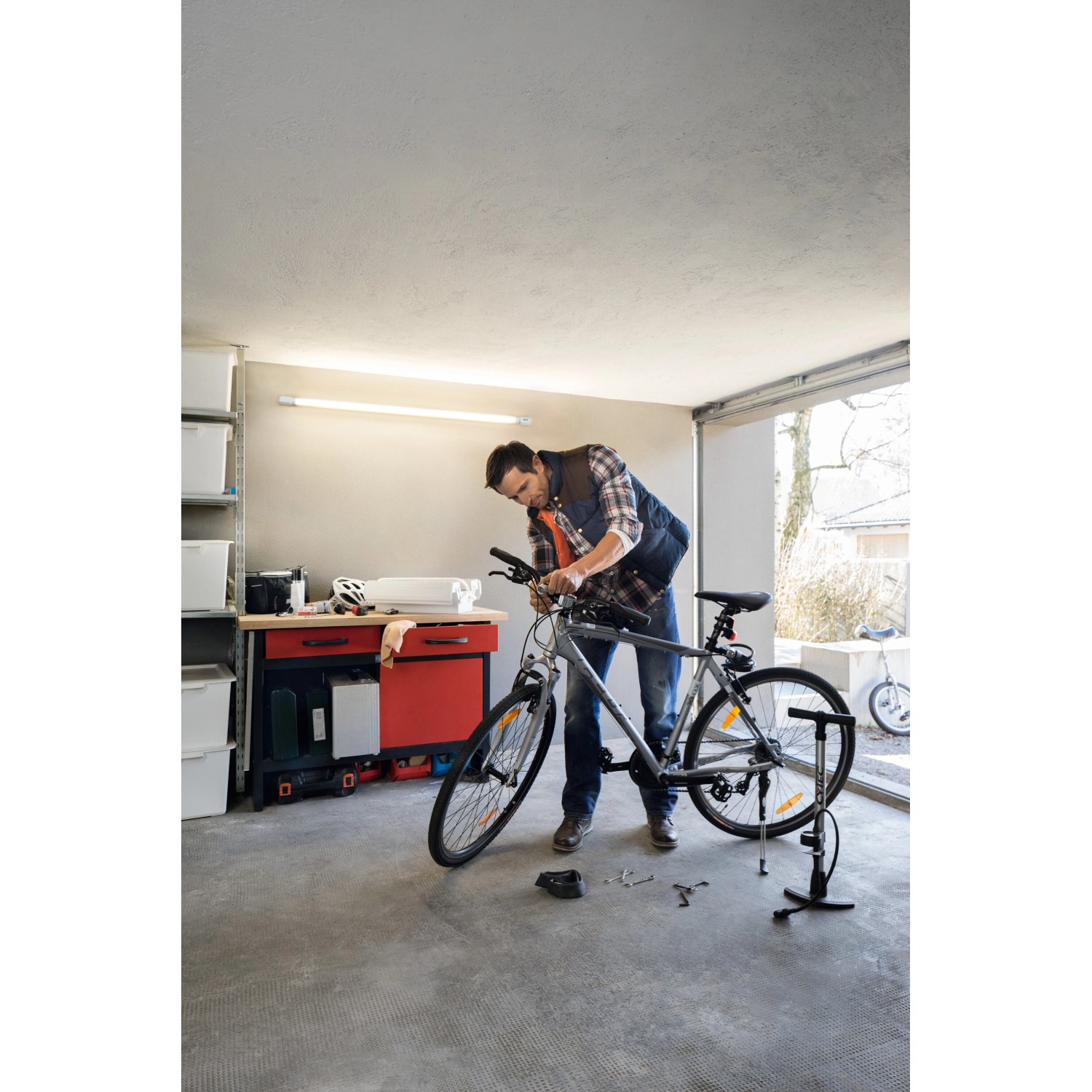 Mann repariert Fahrrad unter Osram LED-Leuchtstofflampe in Garage. Kaltweißes Licht.