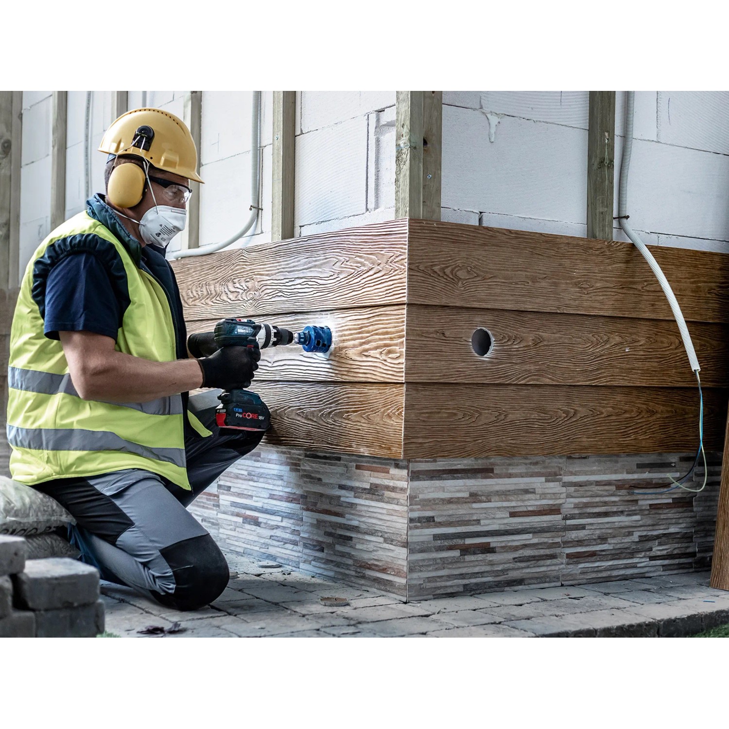 Handwerker bohrt Loch mit Bosch Expert Lochsäge Tough Material Ø 68 mm in Holzverkleidung.