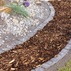 Rindenmulchweg im Garten, umrandet mit Steinen. Natürliche Beetabdeckung mit Rindenmulch.
