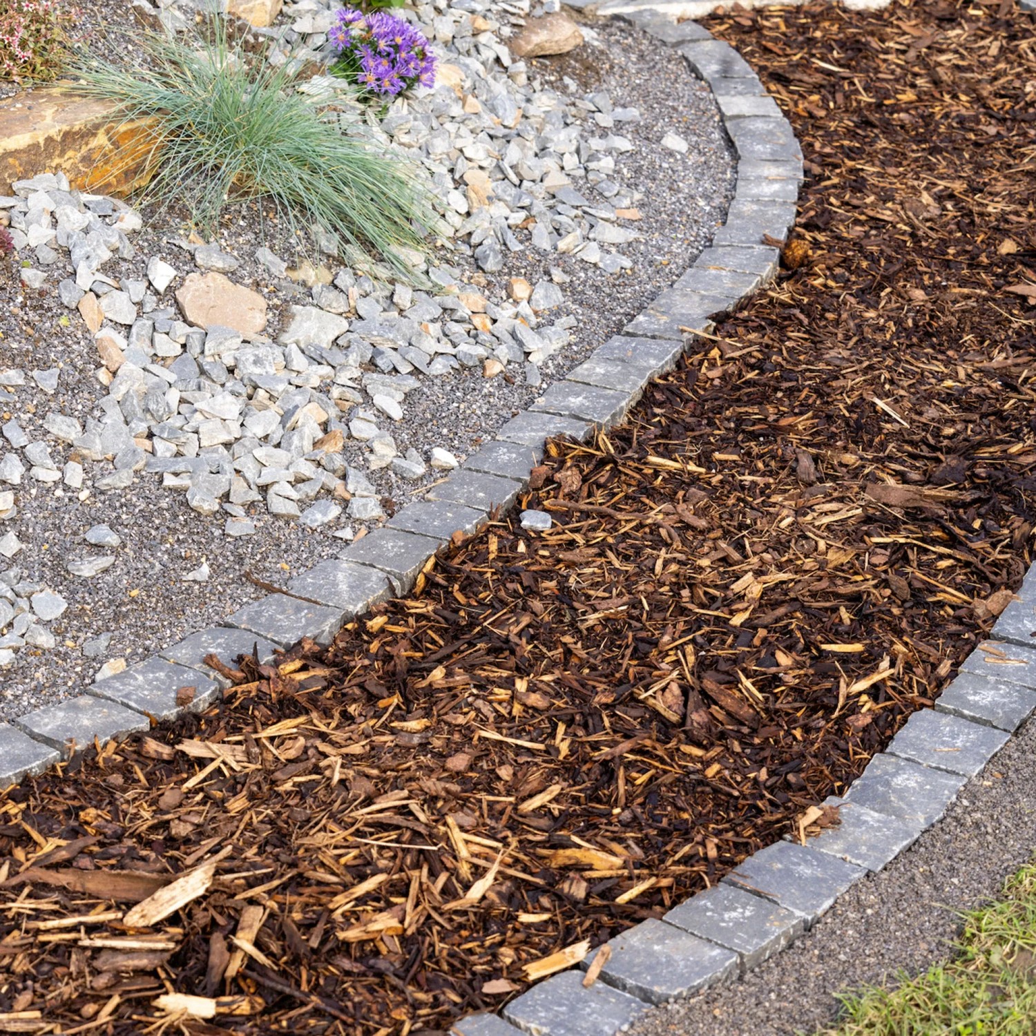 Rindenmulchweg im Garten, umrandet mit Steinen. Natürliche Beetabdeckung mit Rindenmulch.