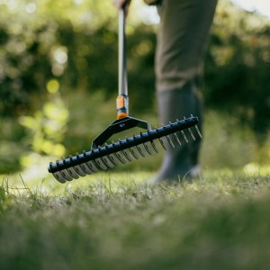 Fiskars Rasenlüfter OneClick im Einsatz auf Rasen, mit Stiel und Zinken zur Moosentfernung.