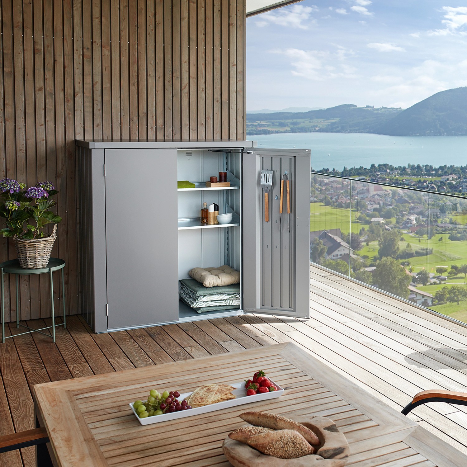 Biohort Geräteschuppen Romeo L, quarzgrau, mit geöffneter Tür und Regalen auf einer Terrasse.