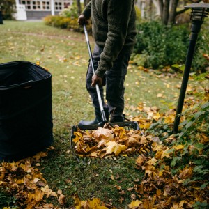 Person harkt Laub mit Fiskars Ergonomic Schaufelrechen und Laubsack im Garten.