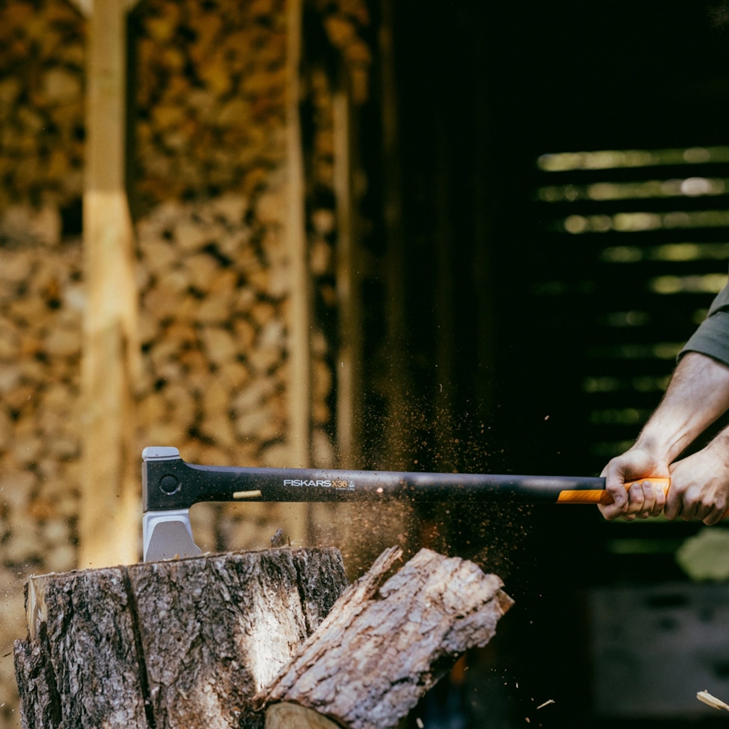 Fiskars X-series Spalt-Axt X36 in Aktion beim Holzspalten vor Holzstapel.