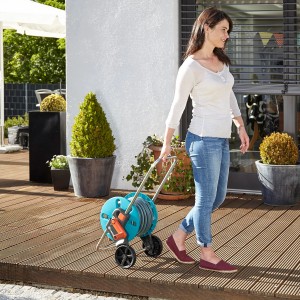 Frau zieht Gardena Schlauchwagen CleverRoll S mit 20m Schlauch über eine Holzterrasse.