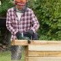 Mann sägt mit Bosch Akku-Kettensäge AdvancedChain 36 V einen Holzbalken im Garten. Trägt Schutzhelm.