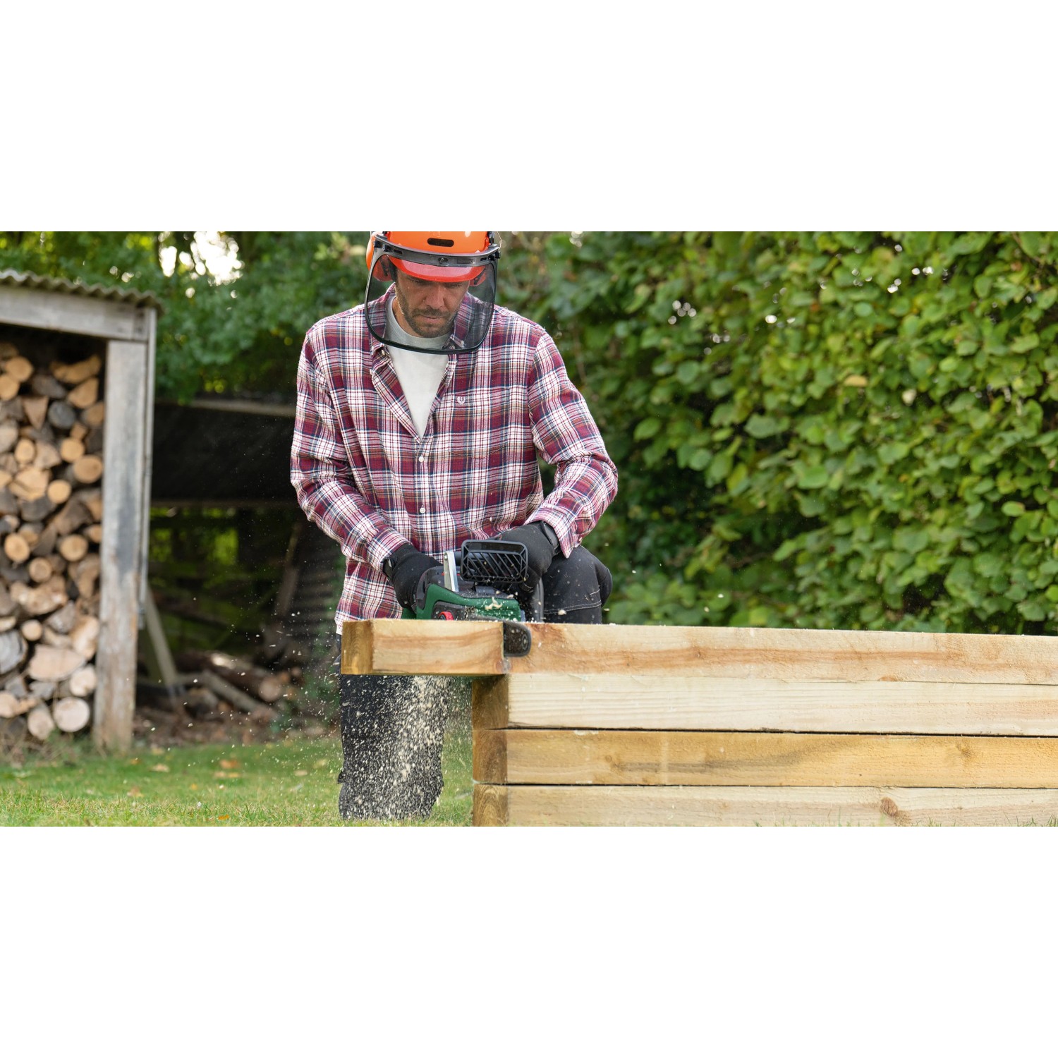 Mann sägt mit Bosch Akku-Kettensäge AdvancedChain 36 V einen Holzbalken im Garten. Trägt Schutzhelm.