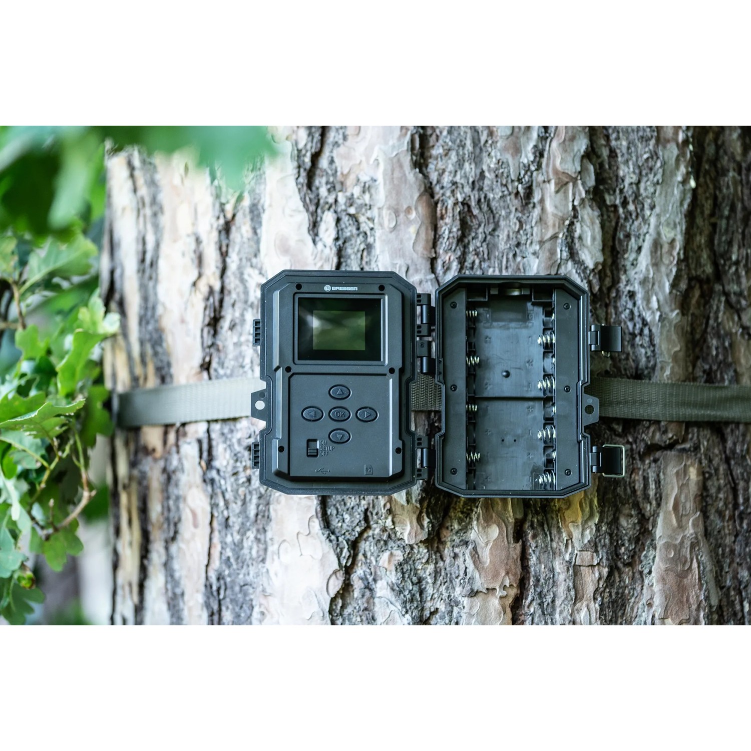 Bresser Wildkamera, 5-20 MP, am Baum befestigt, Gehäuse geöffnet mit Batteriefach sichtbar.