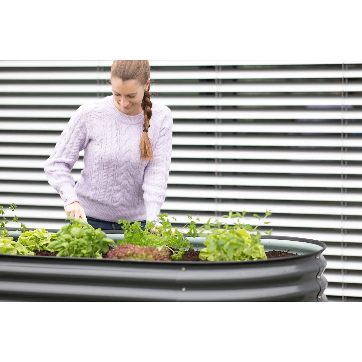 Frau gärtnert im ovalen, anthrazitfarbenen Westmann Metall-Hochbeet (160x80x82cm) mit Salat und Kräutern.