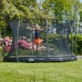 Schwarzes Salta Comfort Edition Bodentrampolin (ø 305 cm) mit Sicherheitsnetz und springendem Kind im Garten.