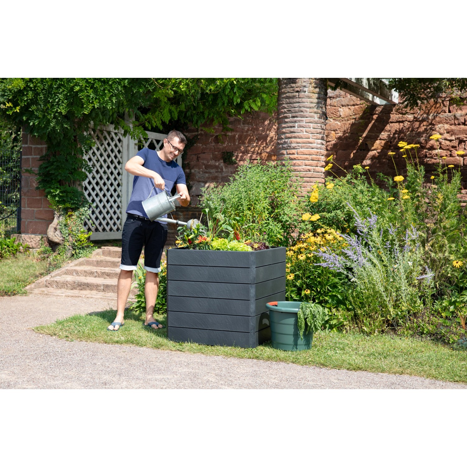 Garantia Hochbeet Ergo Quadro L 75 Stone: Mann gießt Pflanzen im grauen Kunststoff-Hochbeet im Garten.