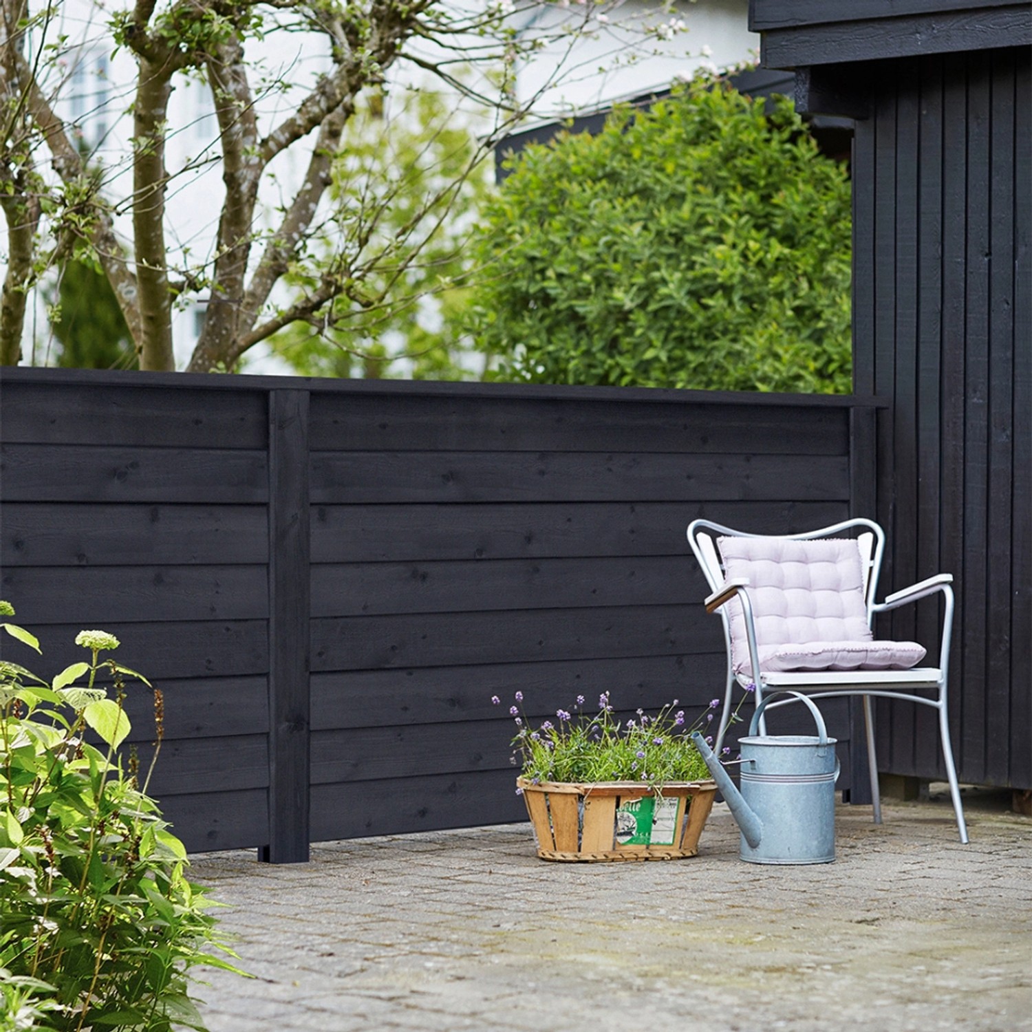 Schwarzer Sichtschutzzaun Klink aus Nadelholz, 174x91cm, im Garten mit Stuhl und Blumen.
