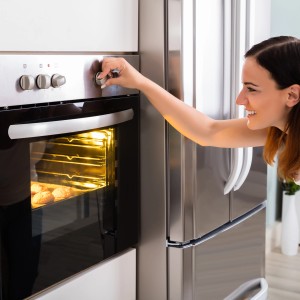 Frau stellt Backofen mit Osram Halogenlampe ein, warmes Licht beleuchtet Backwaren.