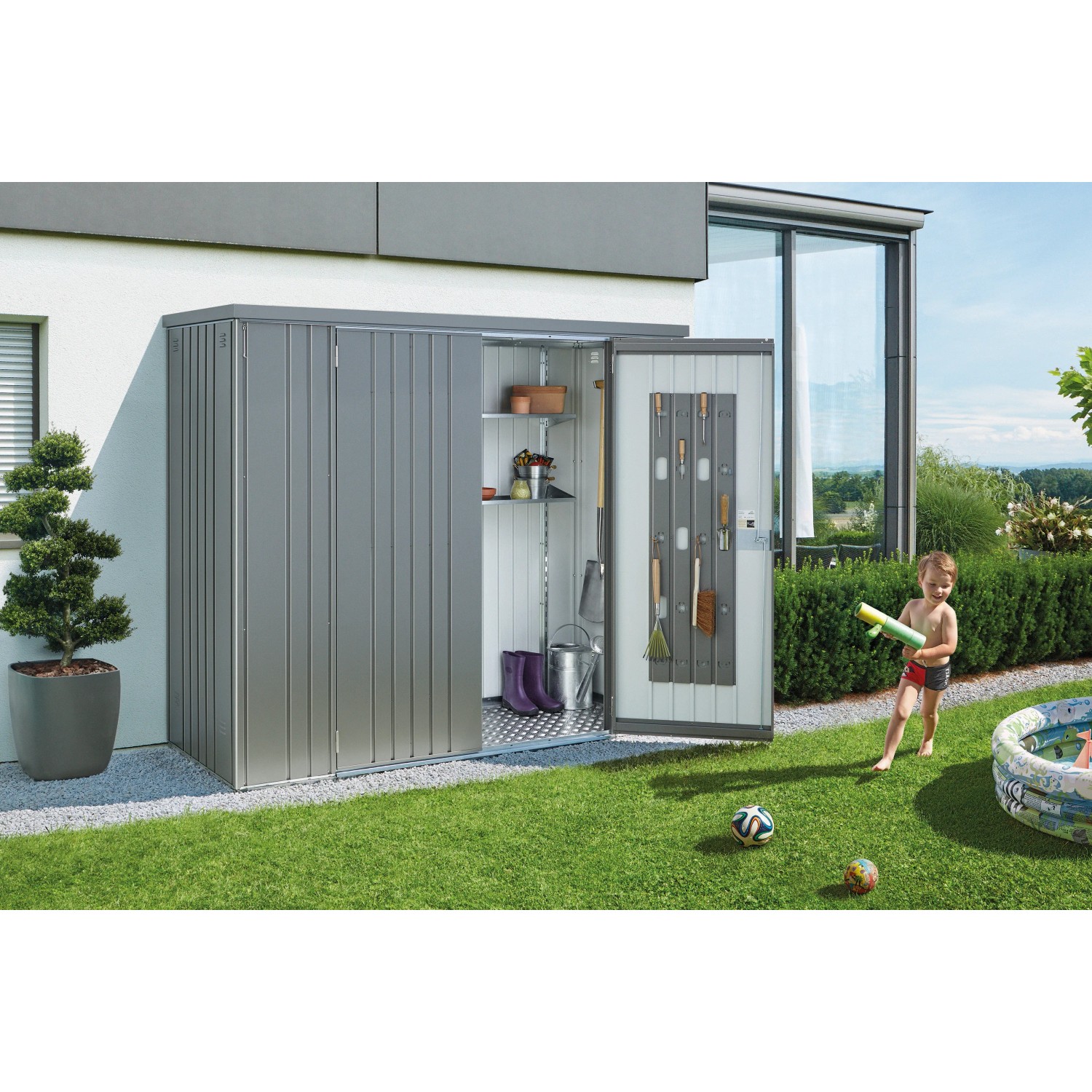 Biohort Geräteschrank Gr. 230, quarzgrau-metallic, mit geöffneten Türen und Zubehör im Garten.