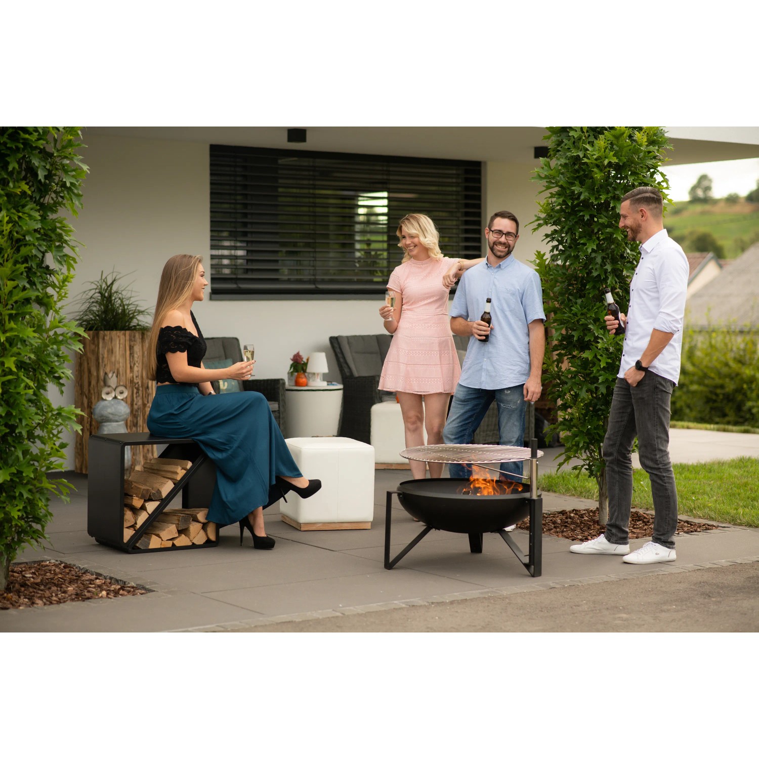 Schwarzes Westmann Kaminholzregal (57x36x56cm) mit Holzscheiten und Person im Garten.
