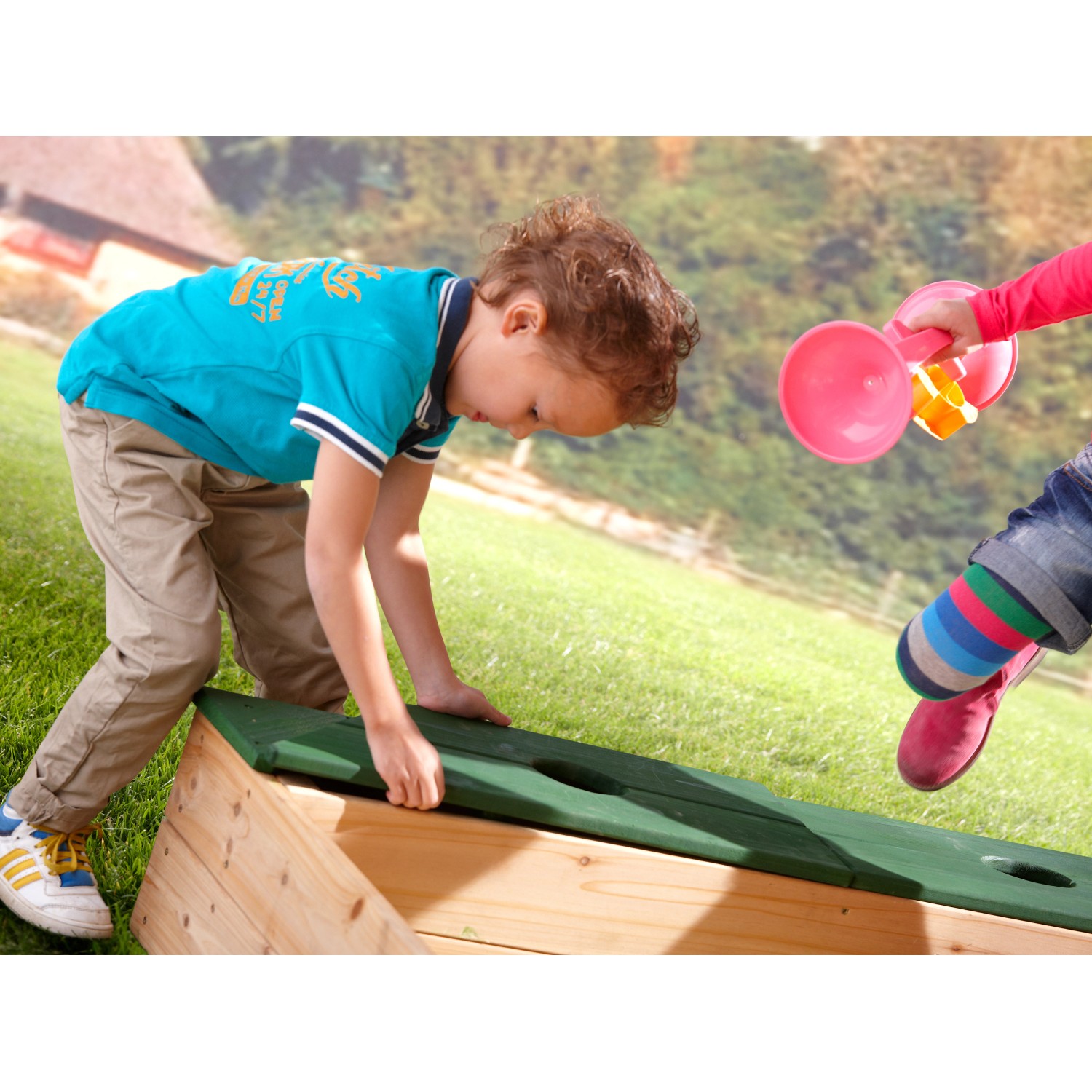 Kind spielt mit Axi Sandkasten Amy 115x115 cm mit Stauraum aus FSC®-Holz.