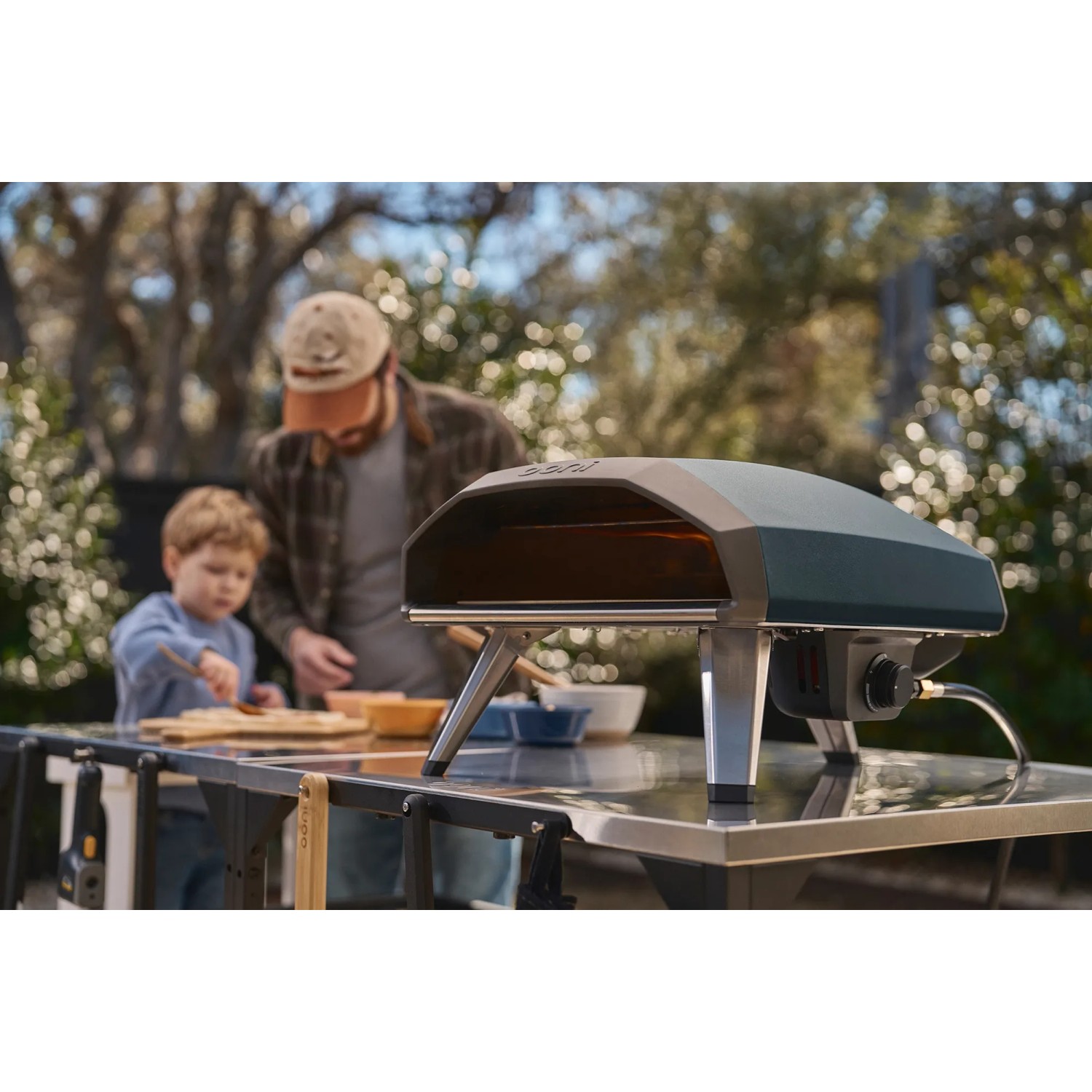 Ooni Gas-Pizzaofen Koda 2 in Schieferblau mit Familie beim Pizzabacken im Garten.
