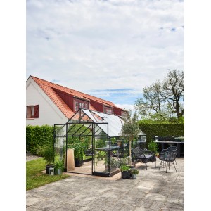 Schwarzes Halls Gewächshaus Qube+ 816 mit 13 m² im Garten, umgeben von Pflanzen.