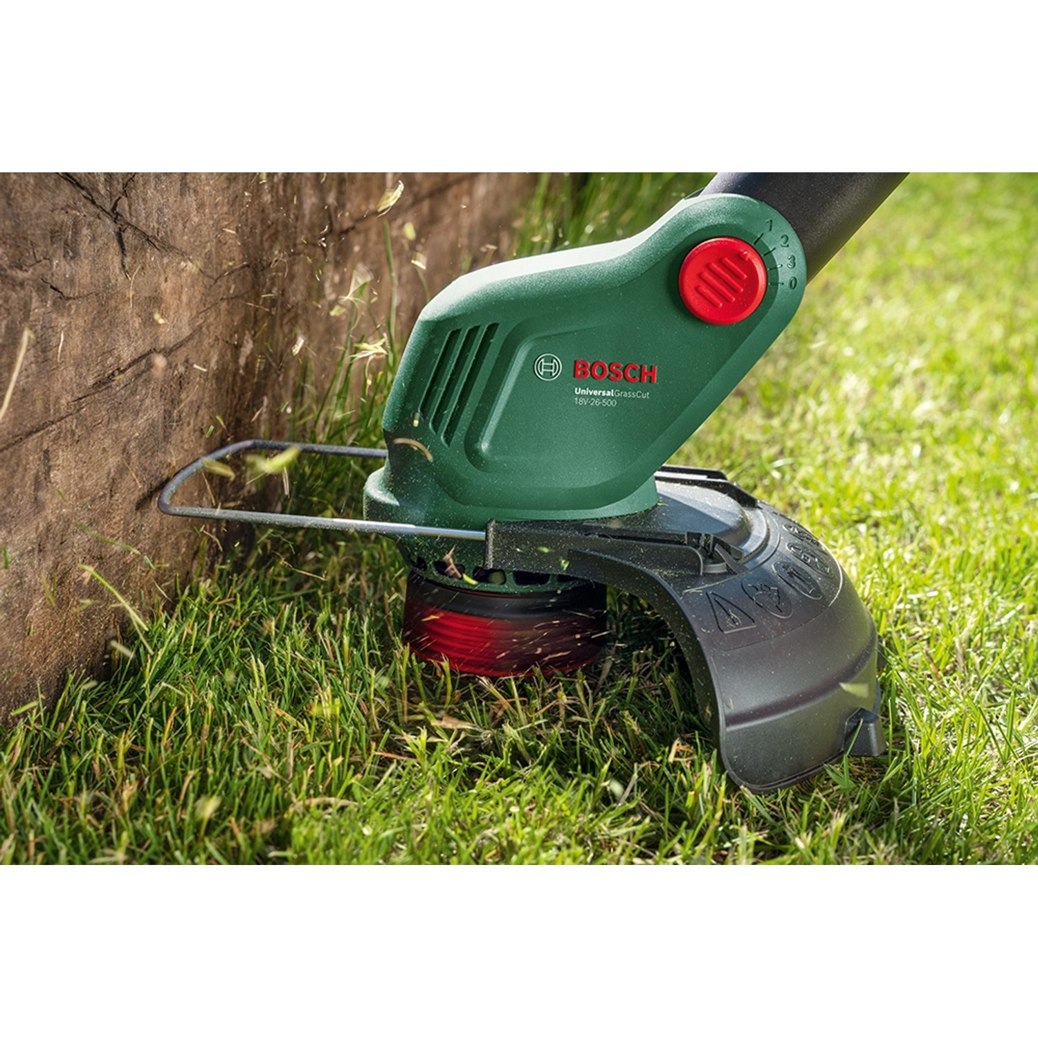 Bosch Akku-Rasentrimmer UniversalGrassCut 18V-26-500 beim Trimmen von Gras an einem Baum.