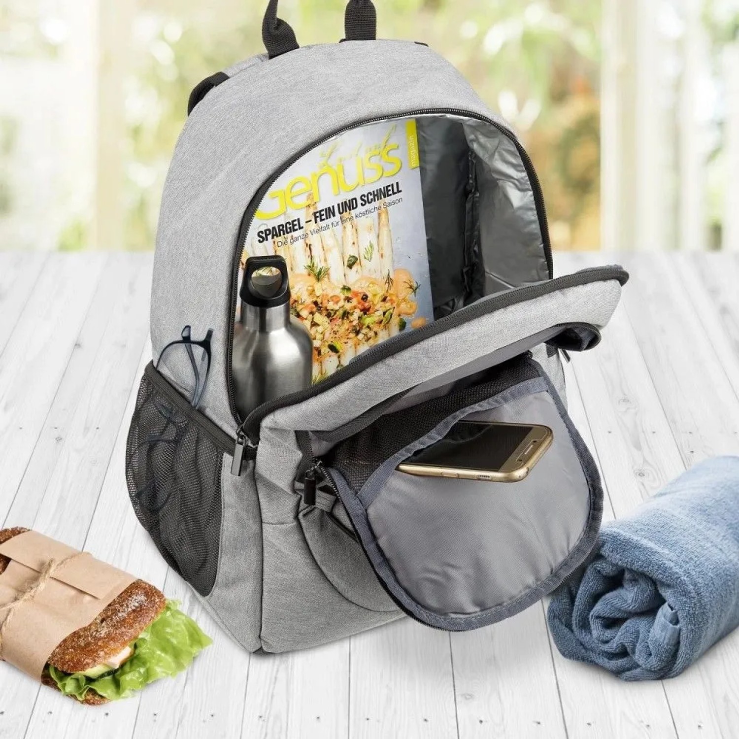 Grauer Bomoe IceBreezer Kühlrucksack (25 Liter) mit Zubehör wie Getränk, Zeitschrift und Smartphone.