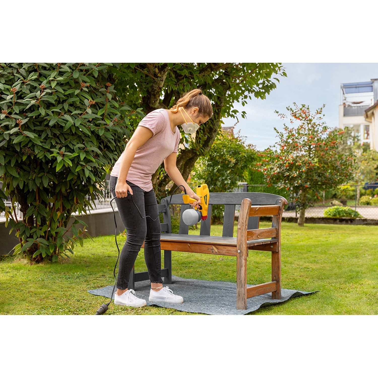 Frau sprüht Holzbank mit Wagner Farbsprühsystem W 125 im Garten.