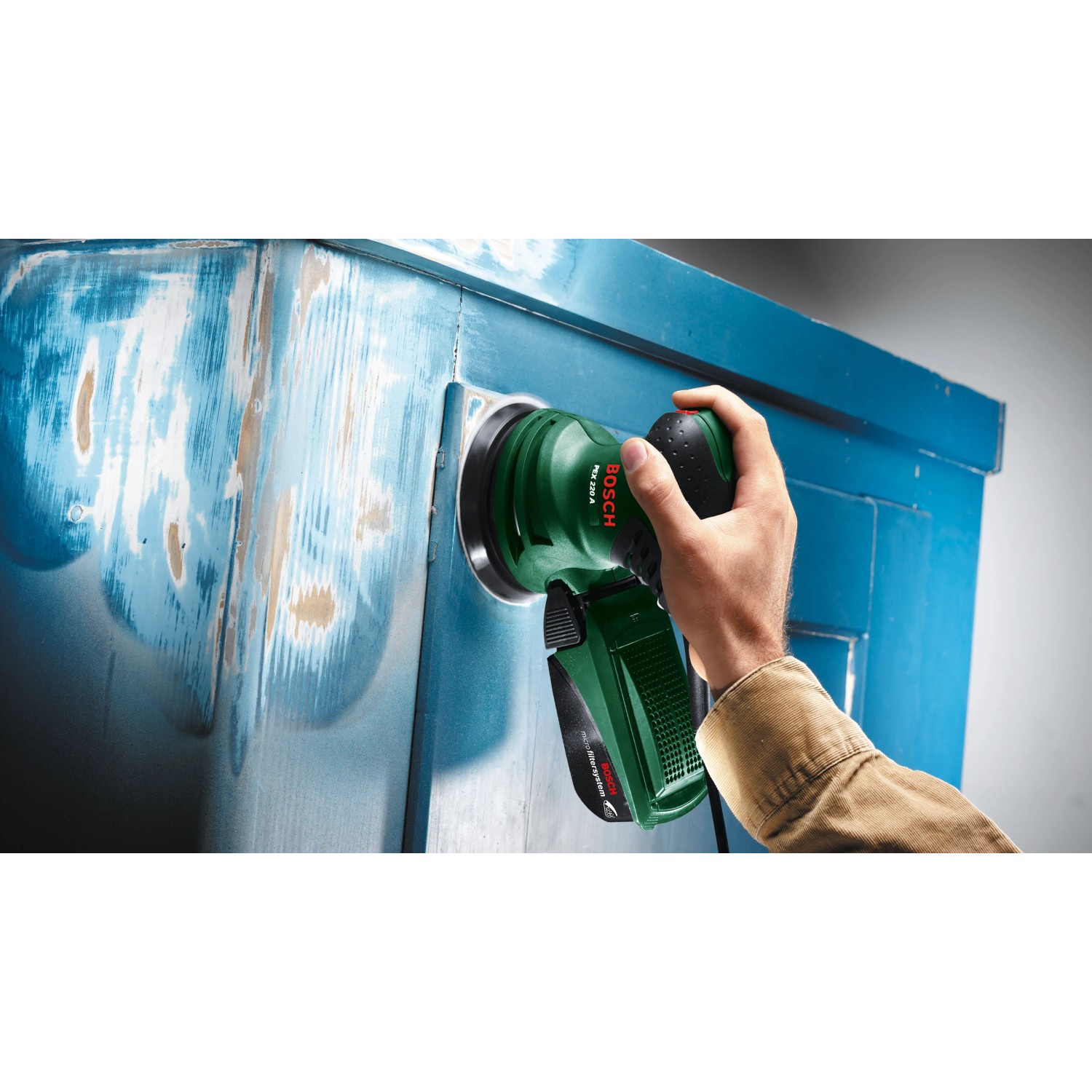 Bosch Exzenterschleifer PEX 220 A schleift blaue Holzmöbel. Grüne Schleifmaschine wird von Hand geführt.
