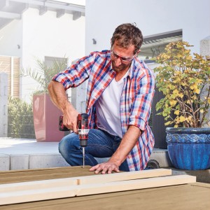 Mann schraubt mit Einhell 12 V Akku-Bohrschrauber TE-CD 12/1 Li im Garten Holz zusammen.