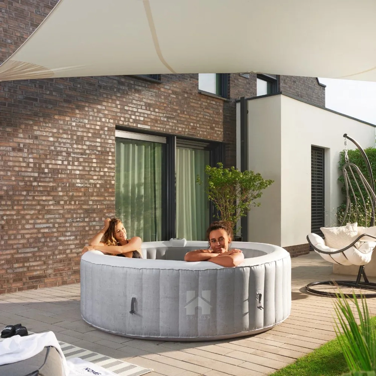 Home Deluxe Whirlpool Splash in Betonoptik mit zwei entspannenden Personen im Garten.