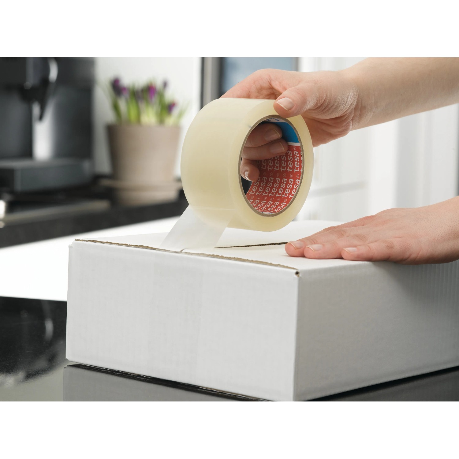 Tesapack Strong Packband beim Verschließen eines Kartons. Braunes Klebeband für sicheren Versand.