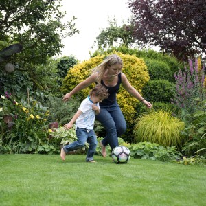 Frau und Kind spielen Fußball auf einem grünen Rasen, gedüngt mit Rasendünger gegen Unkraut und Moos.