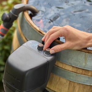 Gardena Akku-Regenfasspumpe 2600 Comfort im Einsatz: Hand stellt Bewässerungsintervalle ein.