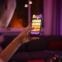 Frau steuert Philips Hue Lampe per App auf Smartphone. LED-Leuchtmittel mit Farbwechsel.