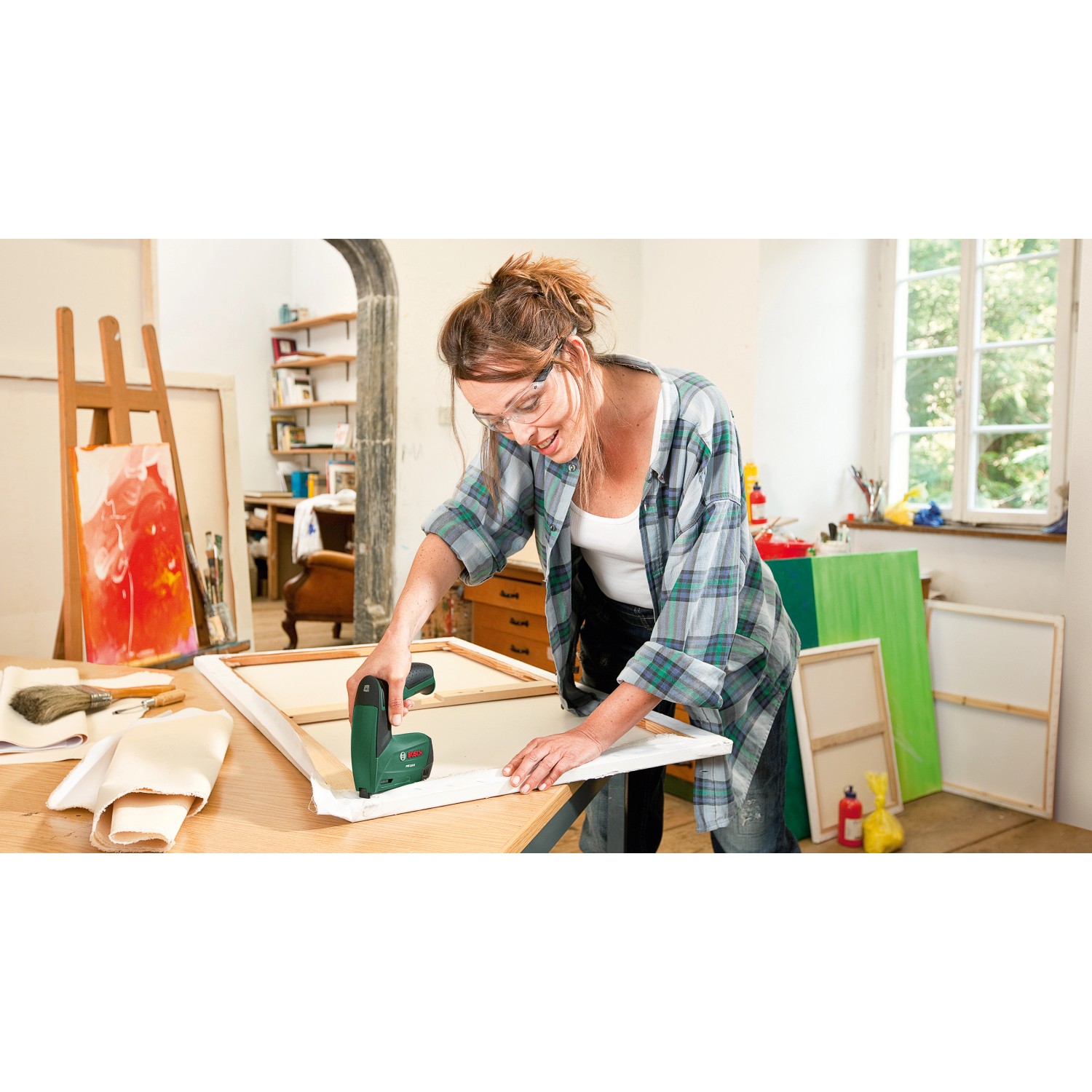 Frau tackert Leinwand mit Bosch Akku-Tacker PTK 3,6 Li. Kabelloser Tacker für Heimwerker.
