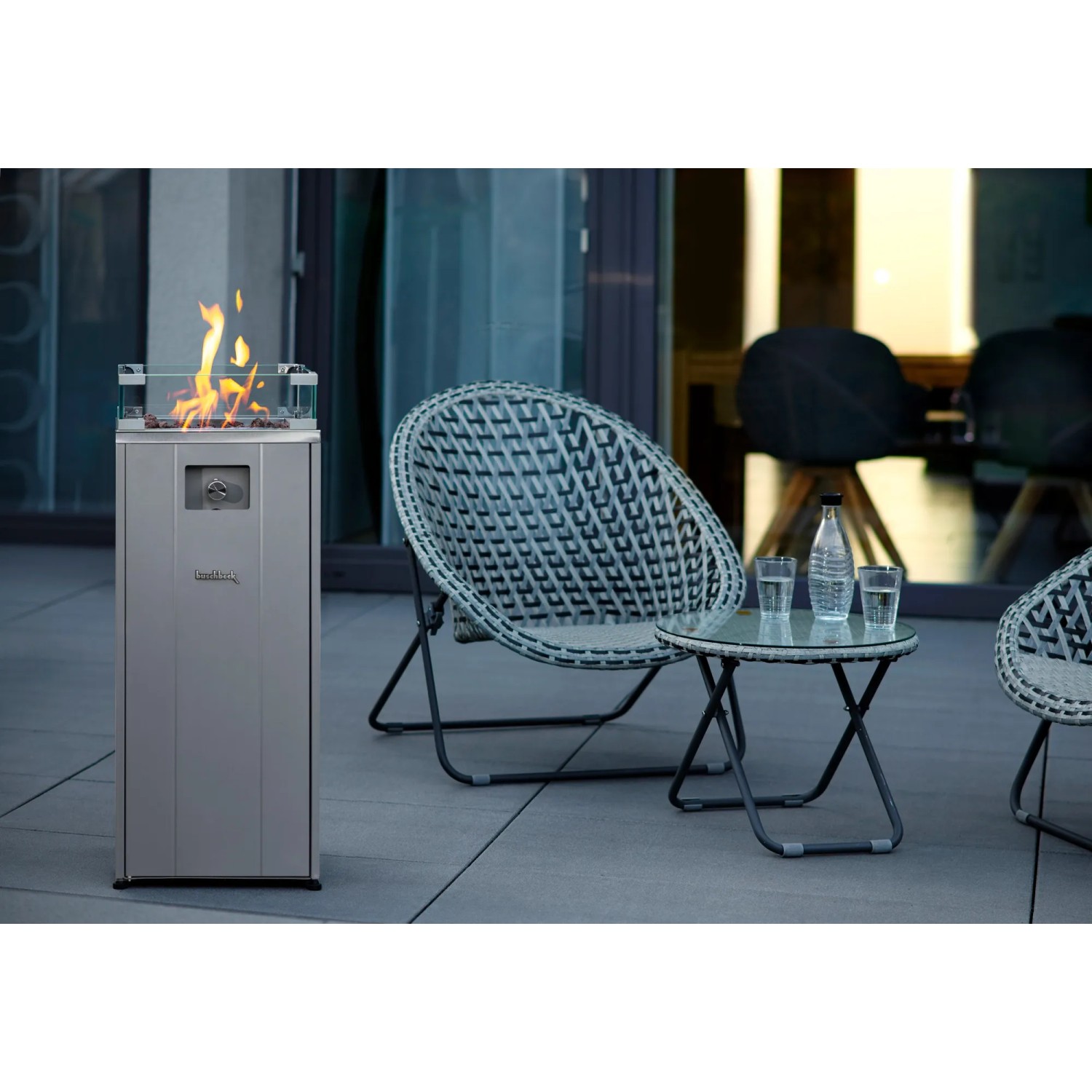 Buschbeck Terrassenheizer Malta Grau mit Glasaufsatz und Flammen, daneben Sitzgruppe.