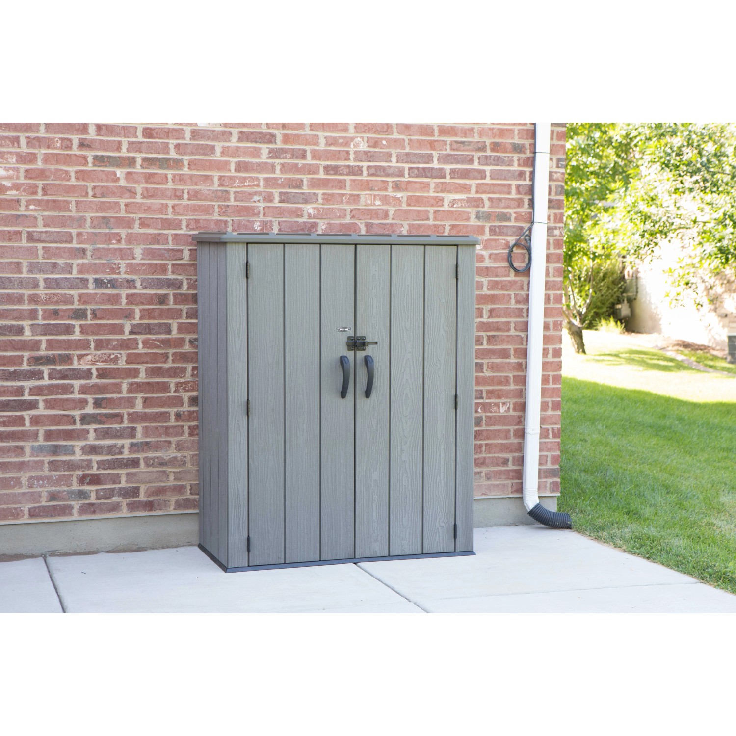 Grauer Lifetime Gartenschrank (136x70x172cm) aus Kunststoff mit Doppeltür vor Backsteinmauer.
