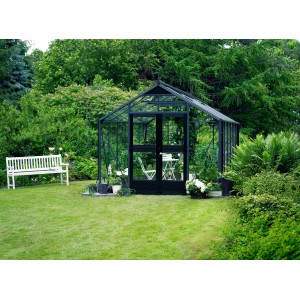 Juliana Gewächshaus Premium 13 Anthrazit (13 m²) im Garten mit Bank und Bewuchs.