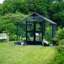 Juliana Gewächshaus Premium 13 Anthrazit (13 m²) im Garten mit Bank und Bewuchs.