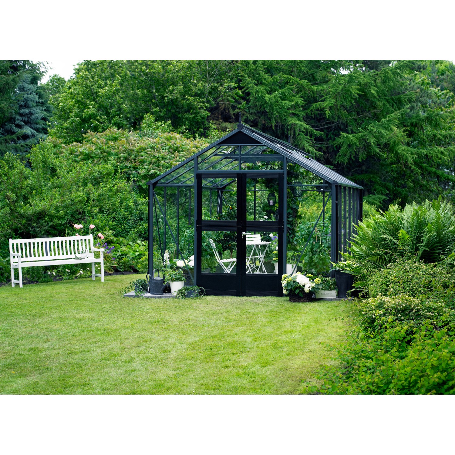 Juliana Gewächshaus Premium 13 Anthrazit (13 m²) im Garten mit Bank und Bewuchs.