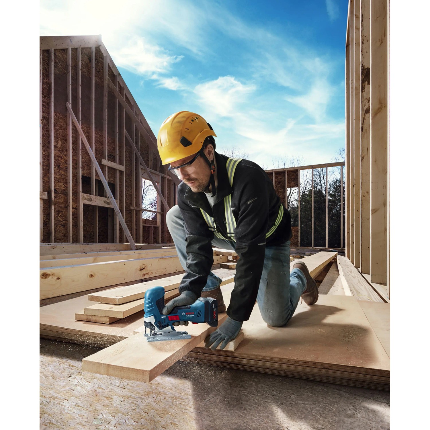 Handwerker sägt Holz mit Bosch Akku-Stichsäge GST 18 V-125 S auf Baustelle unter blauem Himmel.