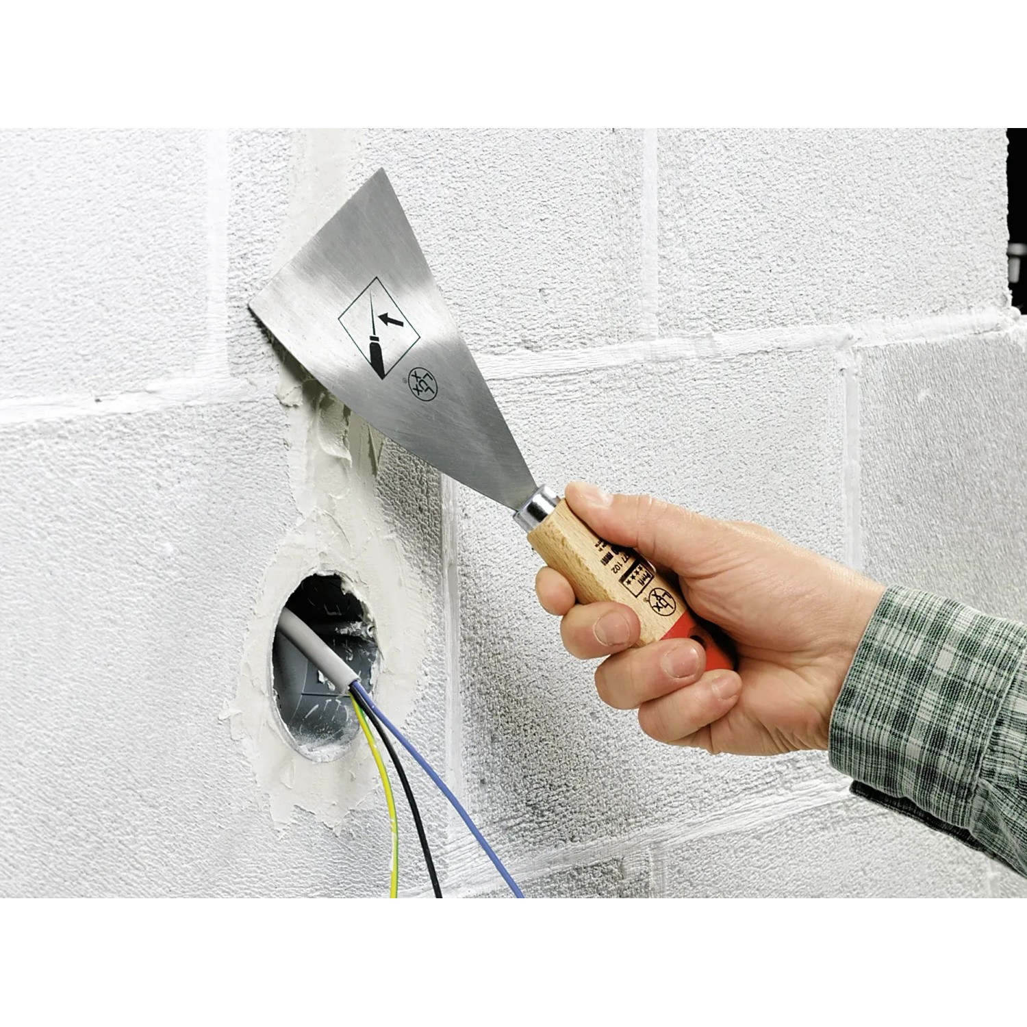 Hand hält LUX Malerspachtel (100mm) zum Glätten von Spachtelmasse an einer Wand.
