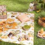 Sommerliches Picknick mit Zitronenmuster: Decke, Kissen, Geschirr, Grill und Getränke im Grünen.