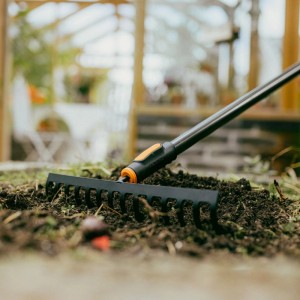Fiskars OneClick Rechen mit 14 Zinken im Einsatz auf einem Beet. Das Kombisystem für die Gartenarbeit.